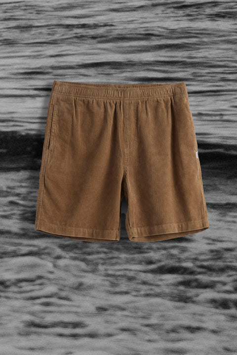 Light brown corduroy shorts with elastic waistband over black and white ocean background.