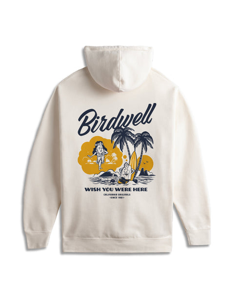 Back view of hoodie in bone. On the back center of the hoodie large screenprinted graphic in navy and yellow of Birdie Daydreaming of Hula Birdie while leaning on a surfboard in front of two palm trees. Navy Birdwell script text above the illustration. Wish You Were Here, California Originals, Since 1961 beneath the illustration. Background is white.