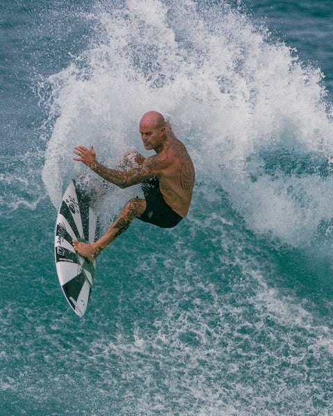 Matt surfing on wave white wearing the 3001 Boardshort in Black. Blue wave in background of image.