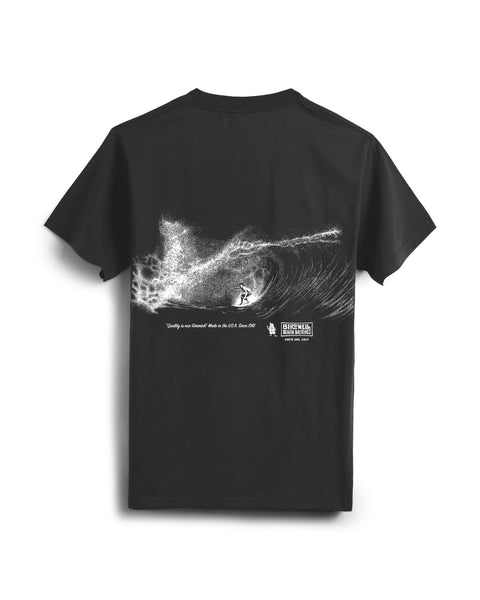 Back of Faded Black T-Shirt on white background with white textural screenprint of surfer on a barrel wave. Beneath the graphic in an italic vintage text saying 