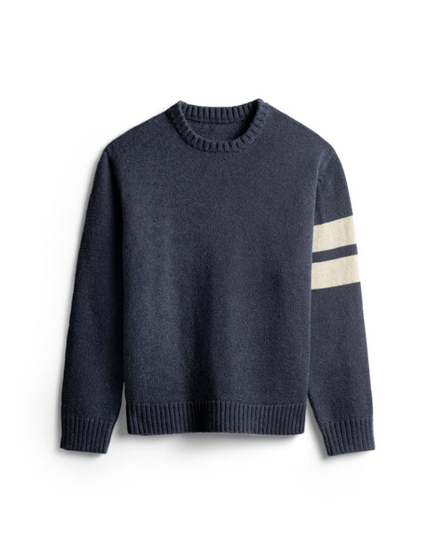 Navy sweater with two horizontal cream stripes on the left arm. Ribbing at collar, sleeves and bottom of sweater. White background.