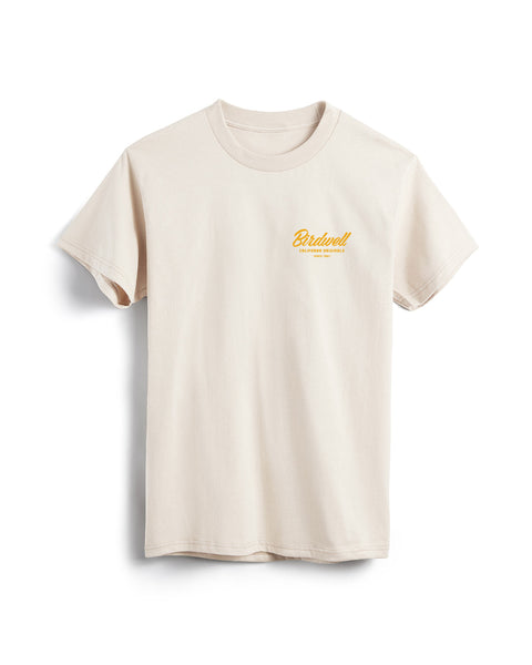 Flatlay of bone colored t-shirt on white background. Graphic on left side of shirt with typographic treatment of Birdwell California Originals Since 1961 in yellow.