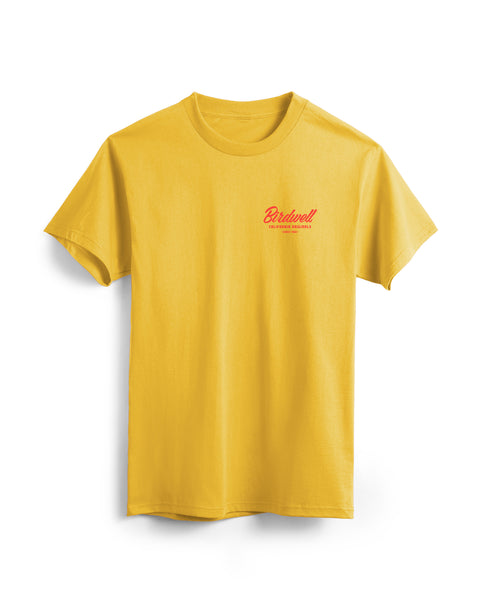 Flatlay of gold colored t-shirt on white background. Graphic on left side of shirt with typographic treatment of Birdwell California Originals Since 1961 in red.