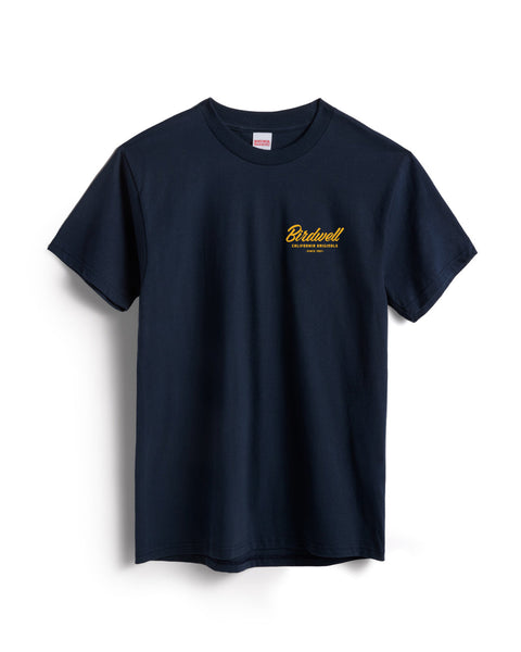 Flatlay of navy colored t-shirt on white background. Graphic on left side of shirt with typographic treatment of Birdwell California Originals Since 1961 in yellow.