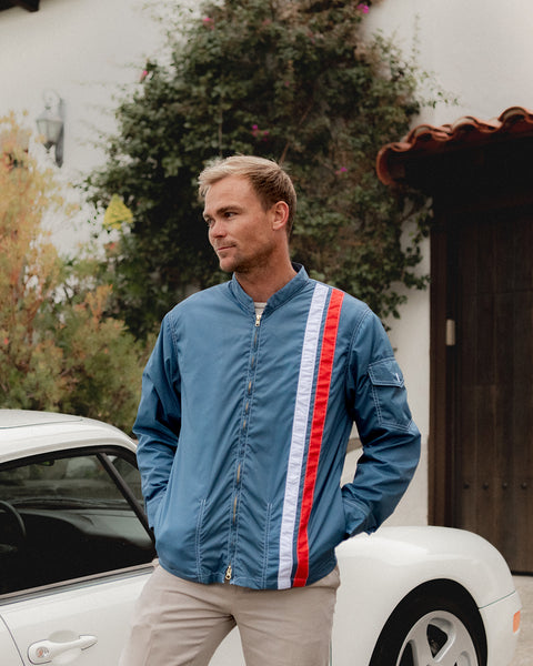 Christian Wach wearing the lemans jacket in federal blue while standing in front of a white sports car with home in background