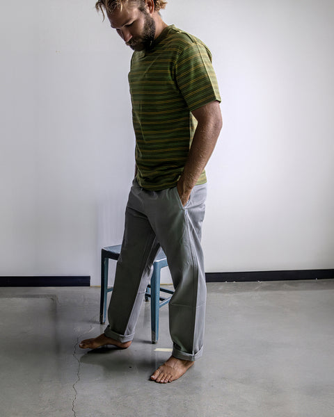 Kevin wearing the Army Green Lowers Shirt and Coronado Pants while standing on cement floor with white wall and blue chair in background.