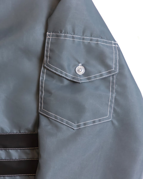 Classic slate pocket detail on sleeve of the jacket with white contrast stitching and white button. Two black stripes with white contrast stitching in lower left of the image.