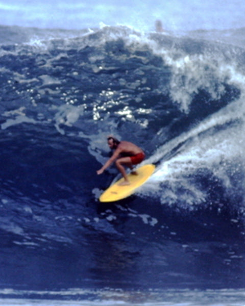 Vintage image of man in red boardshorts surfing on a large wave on a yellow board.