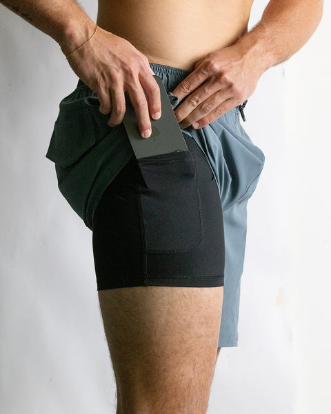 Model wearing the Wright Lined Short in Slate lifting up outer layer of short to reveal compression detail, putting phone in pocket.