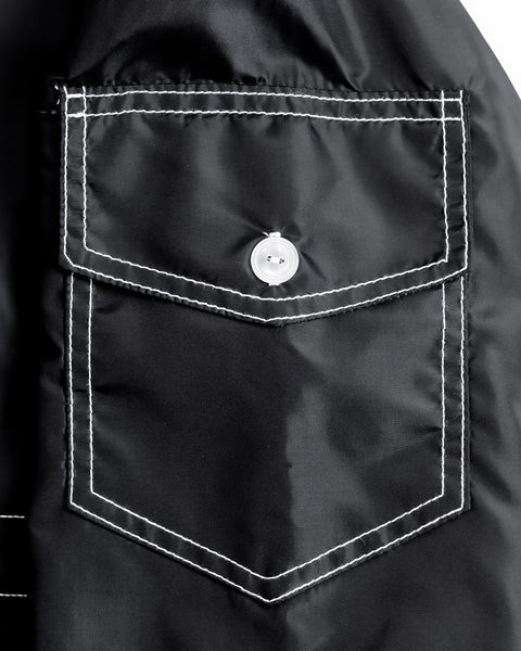 Close up pocket detail from the sleeve of the jacket. Black SurfNyl™ with white contrast stitching and white button.